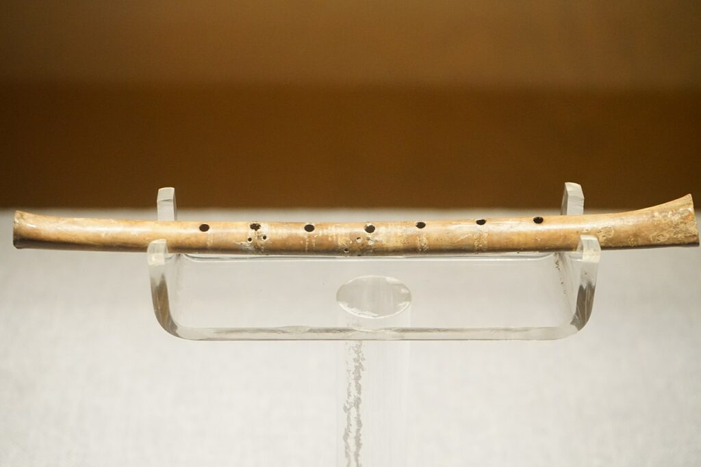 In a clear acrylic stand rests a crane bone flute with 6 finger holes.